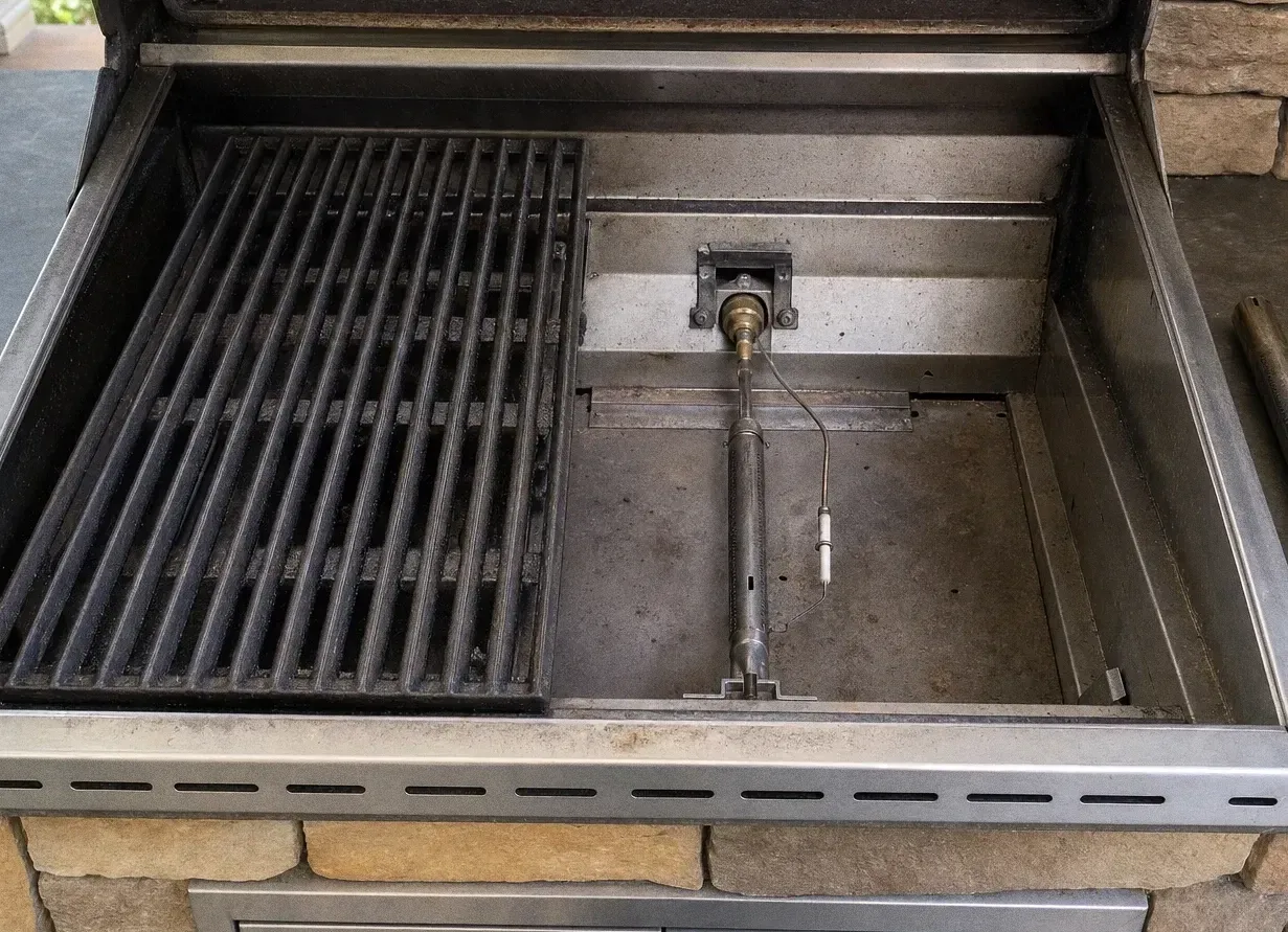 Grill section with one grate lifted clear of the firebox, exposing the burner tube and igniter beneath